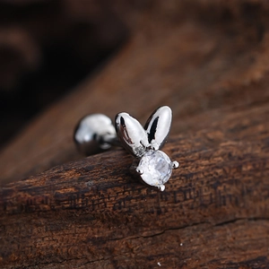 Macro view of silver rabbit ear stud featuring a clear zircon inlay on a dark wood background