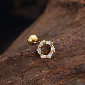 Macro detail of hexagonal gold piercing stud with clear zircon stones on wood surface
