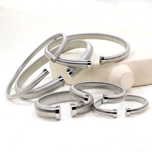 Polished stainless steel spring cuffs in various sizes on a white minimalist stone stand