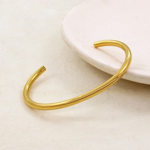 Minimalist C-shaped open bangle in 18K gold finish on a white ceramic plate