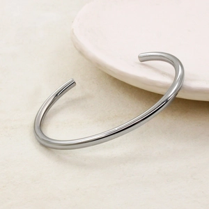 Polished silver C-shaped cuff bracelet with a minimalist mirror finish on a ceramic tray