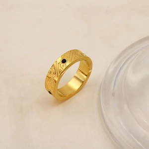 Dettaglio dell'anello in acciaio dorato con motivi floreali incisi e punti neri decorativi