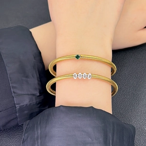 Detailed view of layered gold-tone snake bone bracelets with green and white gemstones