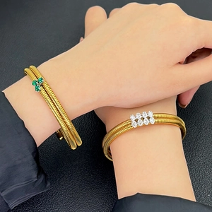 Close-up of golden dual-wrap Tubogas snake bracelets featuring green and white zircons