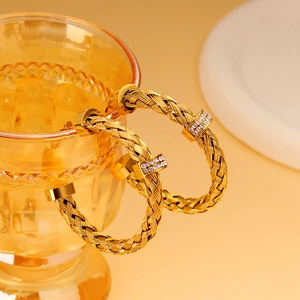 Makroaufnahme von 18k Gold Mesh-Creolen mit funkelnden Strasssteinen auf einem Glas