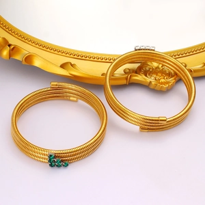 Detail of layered gold spiral bracelets with green and white zircon stones on vintage decor
