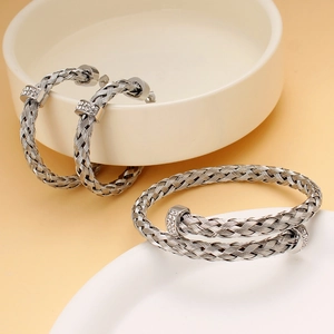 Detail von gewebtem Edelstahlarmband und Ohrring-Set mit glänzenden Diamantakzenten