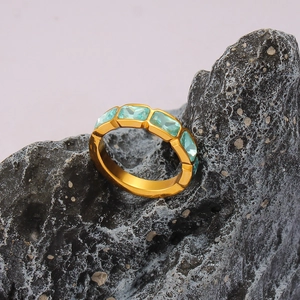 Dettaglio anello dorato con zirconi azzurri rettangolari su pietra naturale