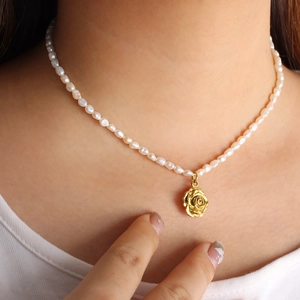 Nahaufnahme einer Perlenkette mit 18K vergoldetem Rosenblüten-Anhänger für Damen