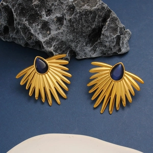 Close-up of vintage golden sunburst earrings with blue teardrop stones on dark rock