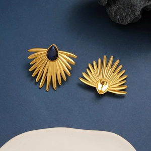 Detail of 18K gold fan-shaped stud earrings with blue teardrop stone on dark rock