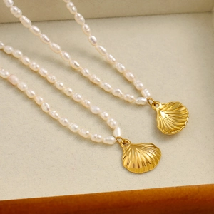 Detail einer Perlenkette mit goldenem Muschelanhänger auf beigem Samtschmuckkästchen
