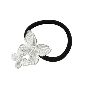 Détail macro du chouchou papillon en métal argenté avec ailes gravées et élastique noir