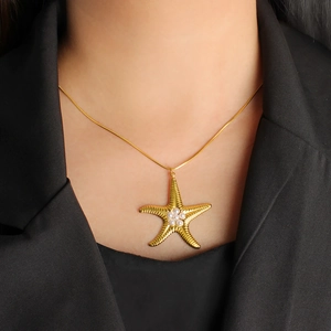 Dettaglio della collana con pendente a stella marina dorata e perle su sfondo nero