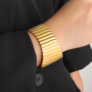 Détail d'un large bracelet manchette plaqué or 18K avec texture ondulée sur le poignet