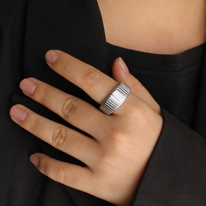 Macro detail of silver-colored wide band ring with vertical stripe texture on model's finger