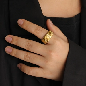 Close-up of wide gold ring with horizontal ridges on finger against black background