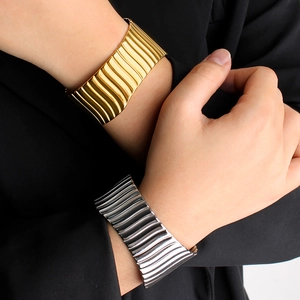 Détail des bracelets larges texturés or et argent portés sur un mannequin en noir