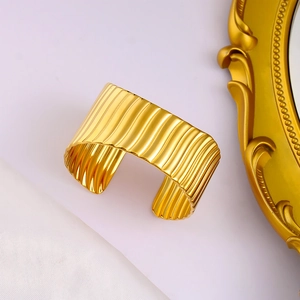 Détail du bracelet large doré avec texture ondulée verticale et finition miroir polie