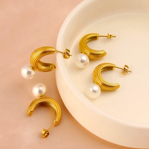 Elegant gold-plated C-shaped earrings with vertical stripes and white pearls in a ceramic tray