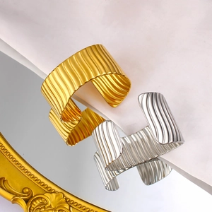 Bracelets manchettes dorés et argentés avec texture ondulée sur une surface miroir