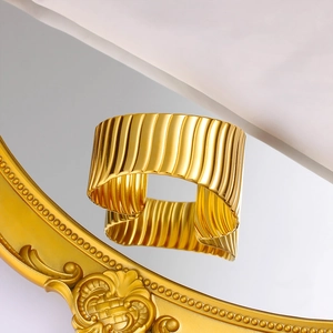Gros plan d'un bracelet manchette doré avec une texture ondulée verticale et un éclat poli