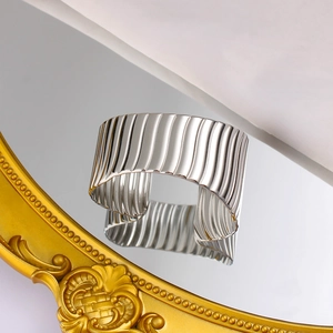 Gros plan d'un bracelet manchette argenté large avec texture verticale sur une surface miroir