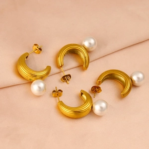 Detailed macro of gold C-shaped hoop earrings with pearls on pink silk fabric