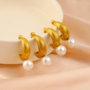 Detailed macro of C-shaped gold pearl earrings with textured metal and small gems