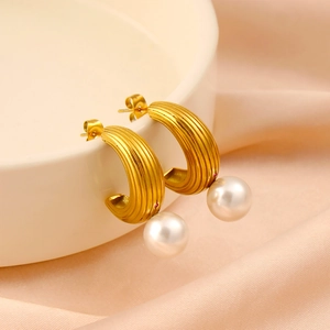 Detailed view of gold C-shaped earring with vertical texture, pearl, and red zircon stone