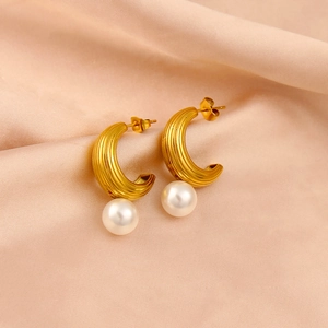 Macro shot of gold C-shaped earrings with vertical texture and white pearl on satin