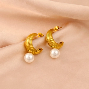 Macro shot of gold C-shaped earrings with textured ribbing and white pearl detail