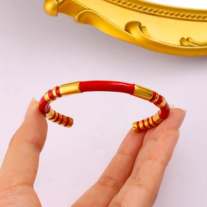 Detailed close-up of golden stainless steel open cuff bracelet with red enamel inlay