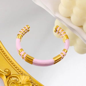 Detail of a C-shaped 18K gold-plated bangle with pink enamel stripes on a reflective surface