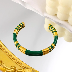 Detail view of a gold-plated C-shaped cuff bracelet with green enamel stripes on a mirror