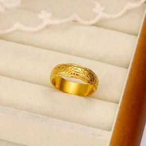 Close-up of a wide 18K gold plated ring with vintage floral engraving on beige velvet
