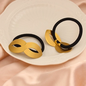 Detailed macro view of matte gold mask charms on elastic hair ties over silk