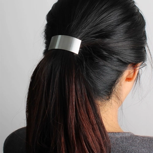 Detail view of rectangular brushed silver metal hair clip on model's black ponytail