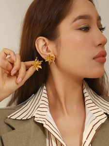 Gros plan de boucles d'oreilles fleurs dorées portées par un mannequin en studio
