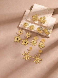 Detalle de pendientes vintage dorados con motivos de flores y conchas sobre piedra