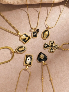 Detailed arrangement of gold-plated necklaces with black enamel religious pendants on sand texture