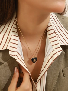Detailed close-up of a black heart pendant with golden daisy on a thin gold bead chain