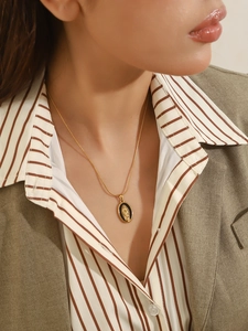 Detail of a vintage gold Virgin Mary pendant necklace worn with a stylish striped shirt