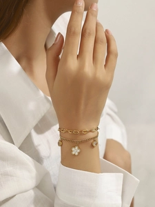 Gros plan d'un bracelet double couche doré avec breloques cœur et fleur blanche au poignet