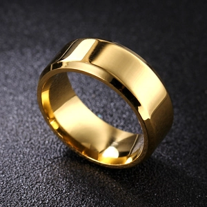 Close-up of polished gold wide-band titanium ring with beveled edges on textured surface