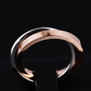 Macro detail of intertwined rose gold and silver stainless steel rings on a black stand