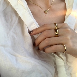 Primo piano di anelli e collana placcati in oro 18K su una modella con luce calda e soffusa