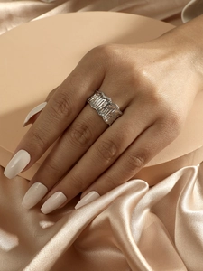 Detail of silver wavy wide band ring featuring sparkling rhinestones on model's index finger