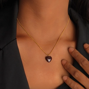 Detail of a 18K gold snake chain with a deep red heart pendant worn on a model