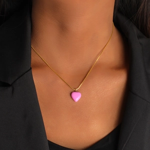 Detail of pink enamel heart pendant on a gold snake chain worn over a black blazer
